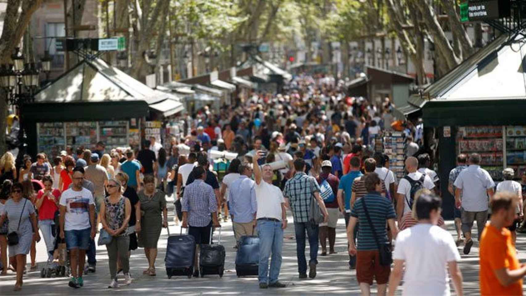 Un turista toma una autofoto en las Ramblas de Barcelona, junto a visitantes con maletas.