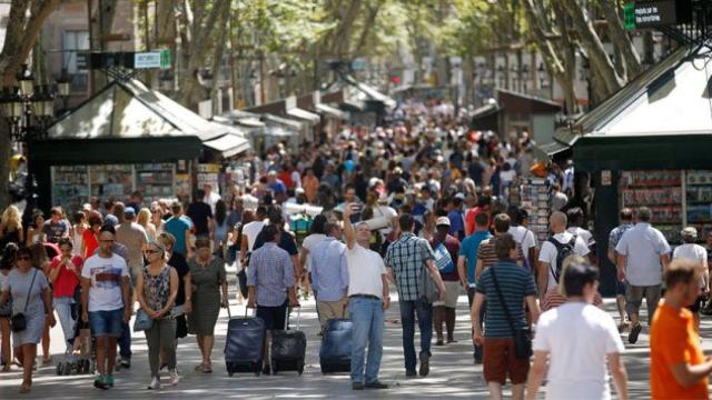 Un turista toma una autofoto en las Ramblas de Barcelona, junto a visitantes con maletas.