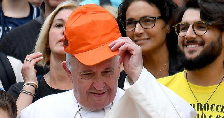 El papa Francisco, muy cercano, se coloca una visera para posar con un grupo de niños durante la audiencia general, este miércoles, en la plaza de San Pedro en el Vaticano / EFE