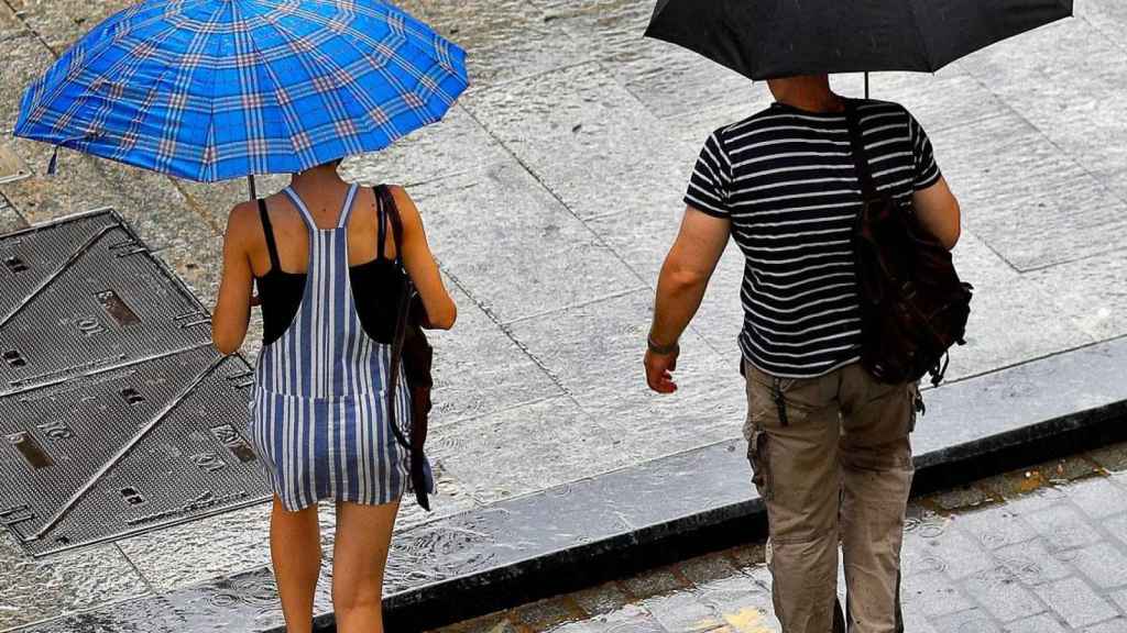 Dos ciudadanos se protegen de la lluvia con paraguas / EFE