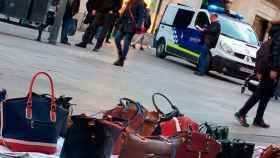 Bolsos a la venta en un 'top manta' en Barcelona junto a una furgoneta de la Guardia Urbana.