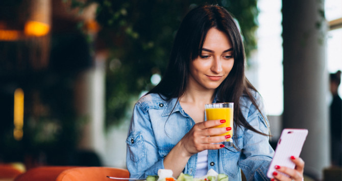 Una chica consulta su móvil mientras desayuna