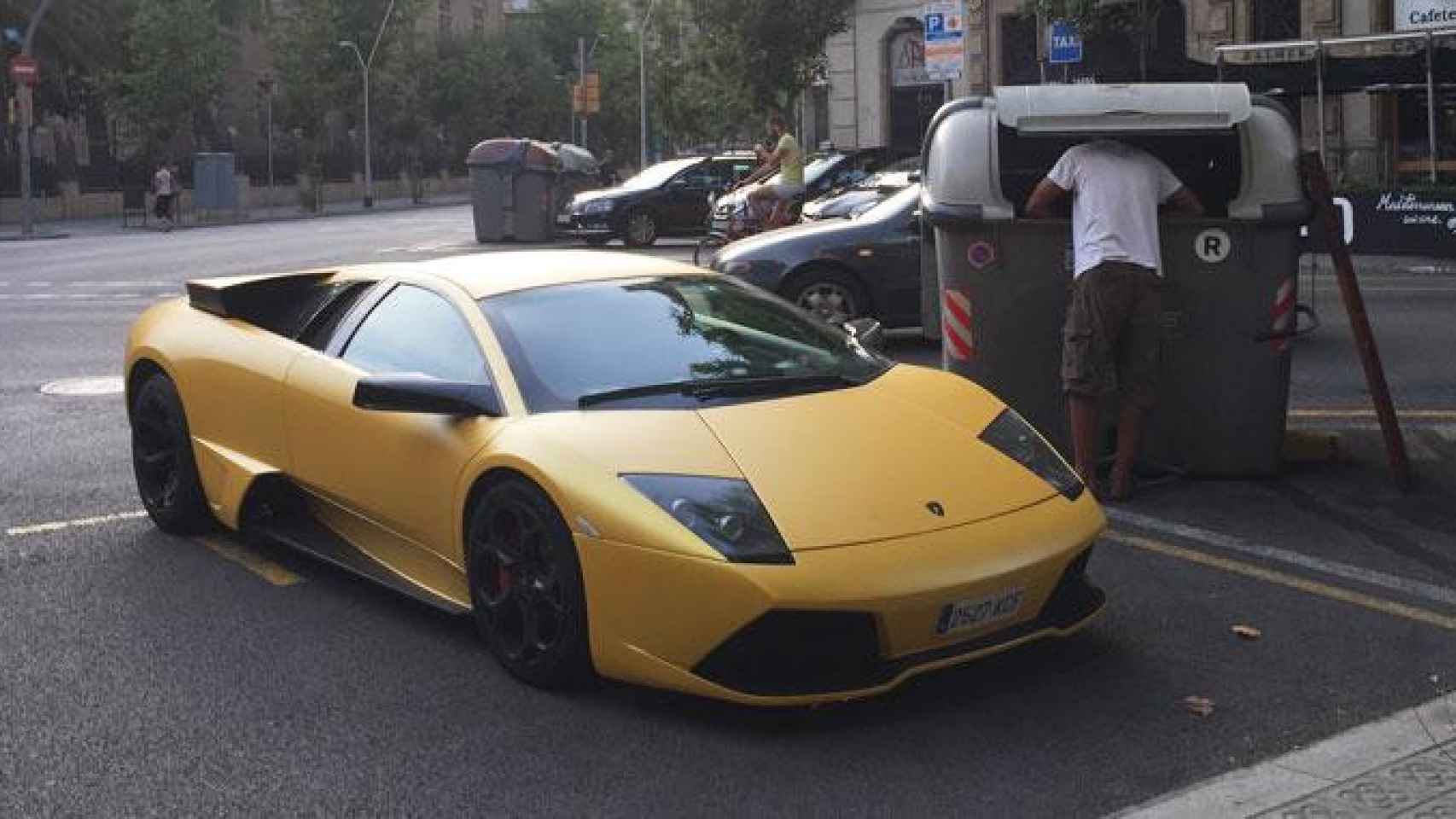 Una persona rebusca en un contenedor al lado de un coche de alta gama en Barcelona / EB