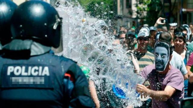 Un okupa del Banc Expropiat de Gràcia lanza un cubo de agua a un agente de los Mossos d'Esquadra / EFE