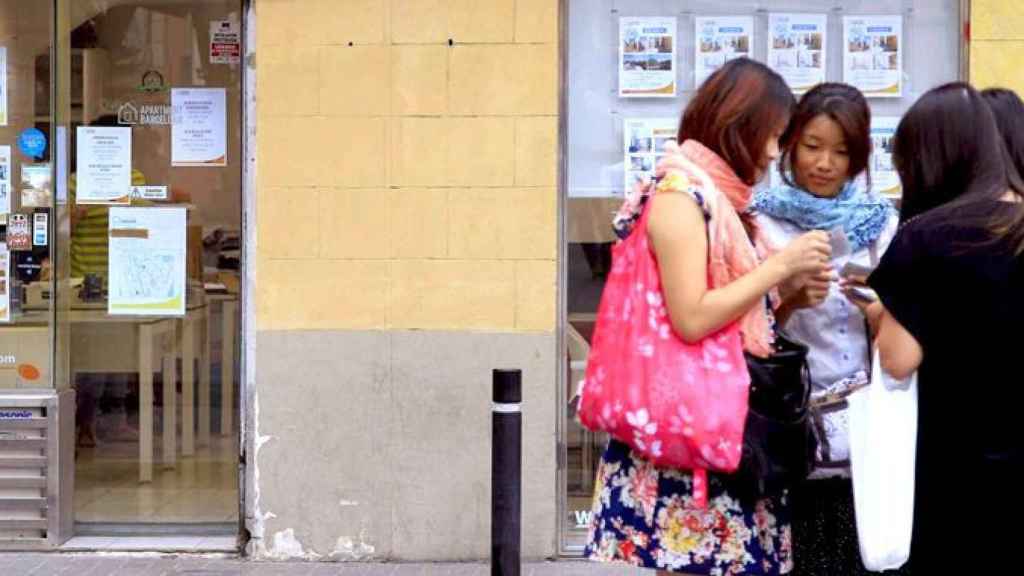 Unas jóvenes charlan frente a una oficina de alquiler de pisos en Barcelona / EFE