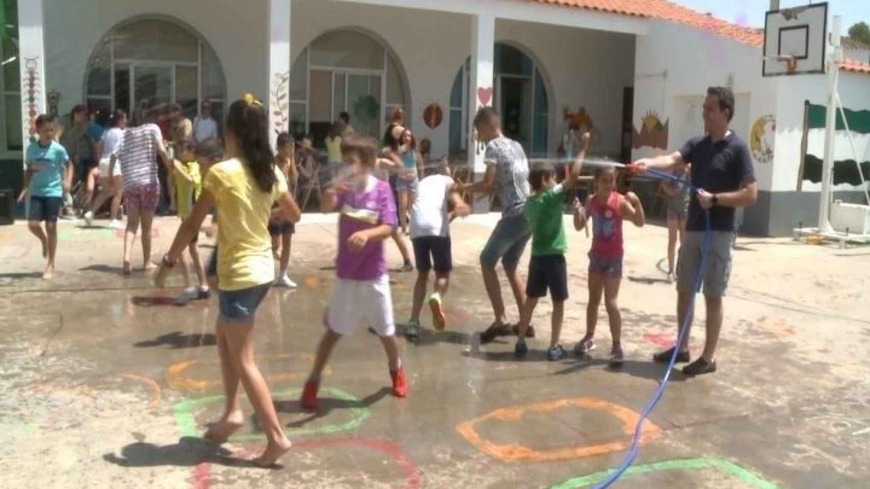 Imagen del patio de un colegio en Andalucía donde un profesor refresca a los niños con una manguera / EUROPA PRESS