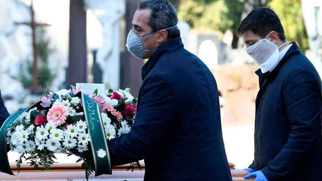 Trabajadores funerarios con mascarilla portando un féretro / EFE