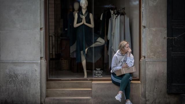 Una mujer sentada ante un escaparate de una tienda de ropa cerrada por no ser comercio esencial / EP