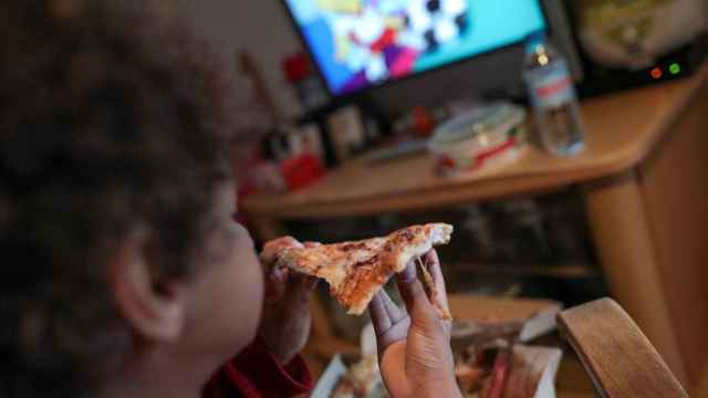 Un niño come una pizza mientras mira canales infantiles en televisión / EP