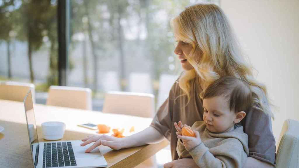 Una mujer teletrabaja con un niño en brazos / PEXELS