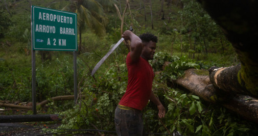 Un hombre intenta hoy cortar un enorme árbol que bloquea la carretera de acceso a Samaná / Orlando Barría – EFE