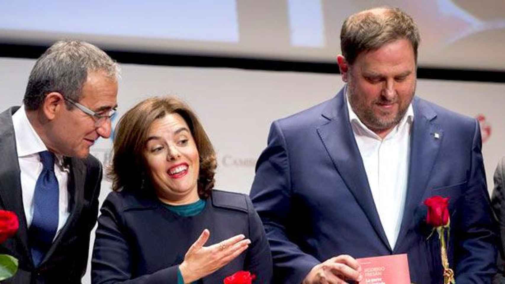 La vicepresidenta del Gobierno, Soraya Sáenz de Santamaría (c), regala un libro al vicepresidente de la Generalitat de Cataluña, Oriol Junqueras (d), por Sant Jordi bajo la mirada del presidente del Gremio de Libreros, Patrici Tixis (i) / EFE