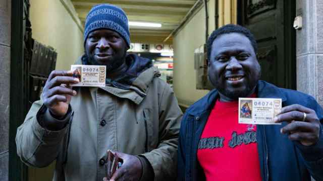 Dos ciudadanos gambianos enseñan sus números premiados en el sorteo de la Lotería de Navidad / EFE