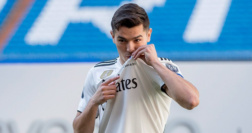 Brahim Díaz, vestido de blanco en el césped del estadio Santiago Bernabéu, besa el escudo madridista durante su presentación como futbolista del Real Madrid / EFE