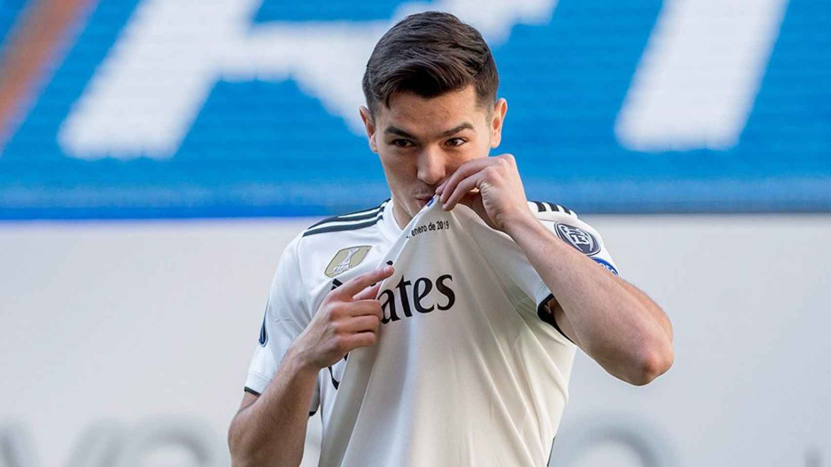 Brahim Díaz, vestido de blanco en el césped del estadio Santiago Bernabéu, besa el escudo madridista durante su presentación como futbolista del Real Madrid / EFE