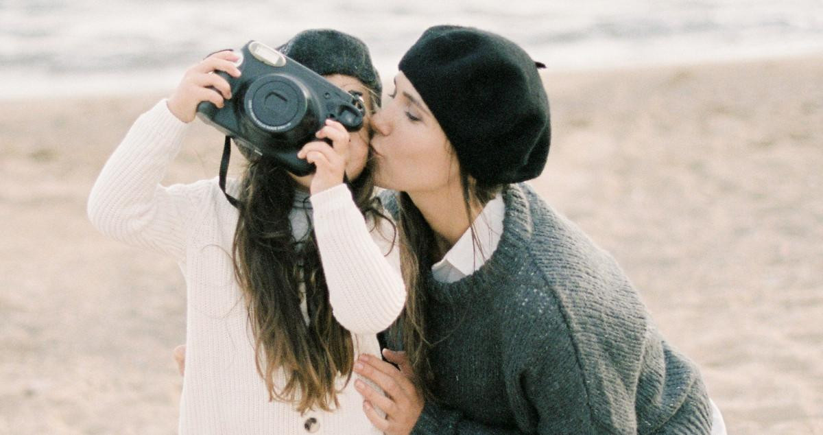 Una madre besa a su hija mientras hacen fotografías en una playa / PEXELS