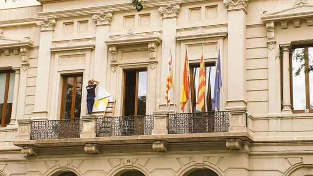 Un operario retira el lazo amarillo de la sede del Ayuntamiento de Barcelona en Les Corts / CS