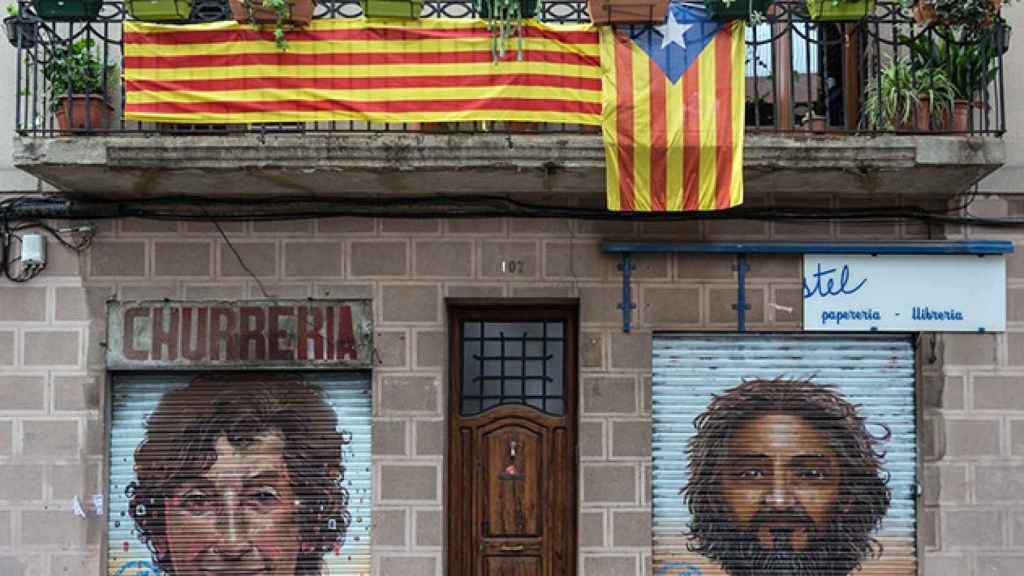 Un balcón con una senyera y una 'estelada' sobre dos comercios cerrados