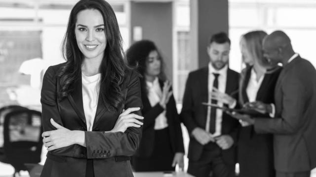 Una mujer empresaria mira a cámara en la oficina con su equipo detrás / EP