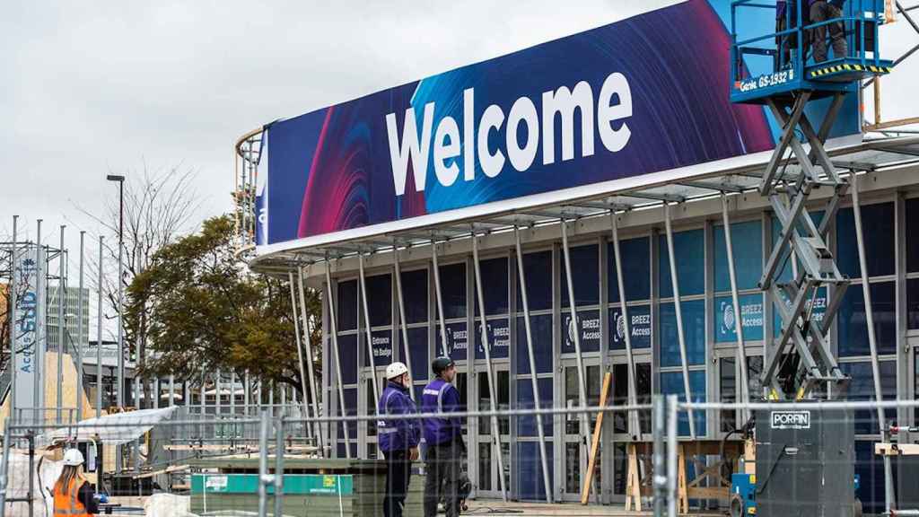 Dos trabajadores subidos a una plataforma elevadora colocan un cartel en el que se lee 'Welcome' en el exterior de la entrada principal del pabellón del evento Mobile World Congress / EP