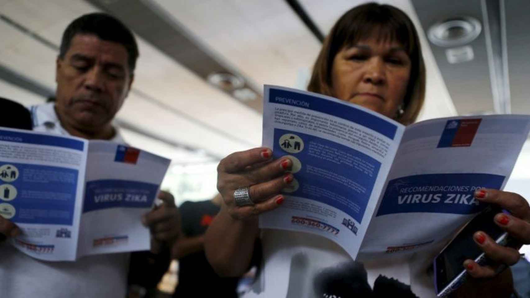 Dos pasajeros consultan material de información contra el zika en un aeropuerto.