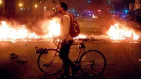 Un joven pasea con su bicicleta, en Barcelona, junto a las barricadas en llamas de una manifestación independentista / C.G.