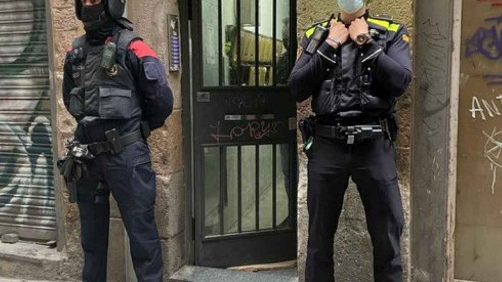 Un agente de los Mossos y otro de la Urbana en la entrada del bloque donde se encontraba el 'narcopiso' desmantelado en el Raval / GUARDIA URBANA