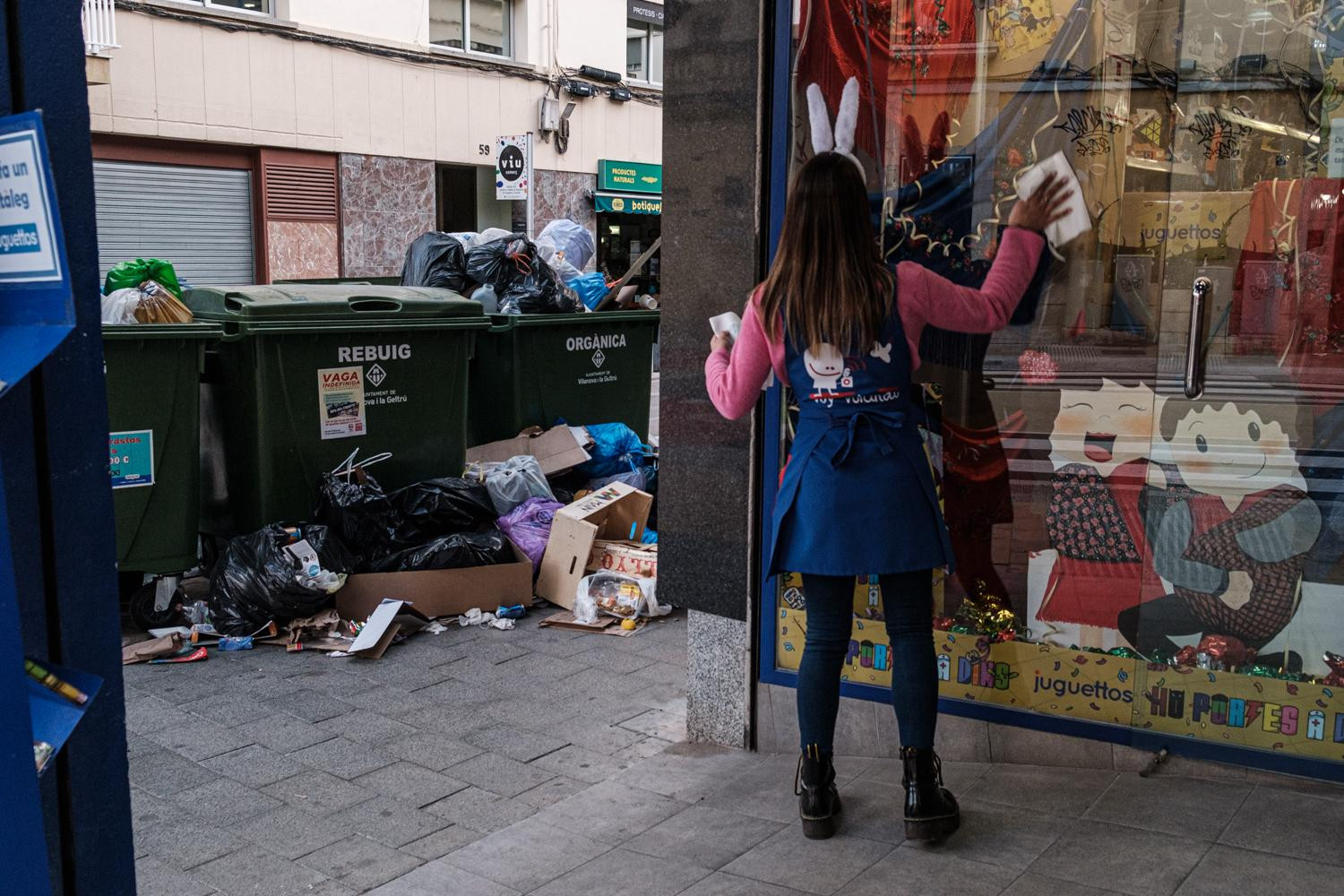 Una trabajadora limpia los cristales de su tienda rodeada por basura / PABLO MIRANZO