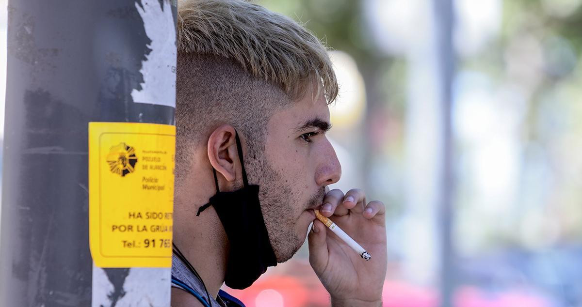 Un joven con la mascarilla bajada para poder fumar / EP