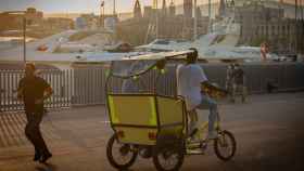 Un bici-taxi para turistas pasa por delante de los yates del Puerto de Barcelona / EP