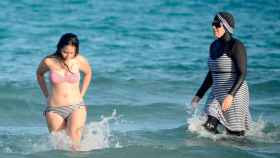 Una mujer se baña con un burkini frente a otra, que lo hace en bikini / AFP