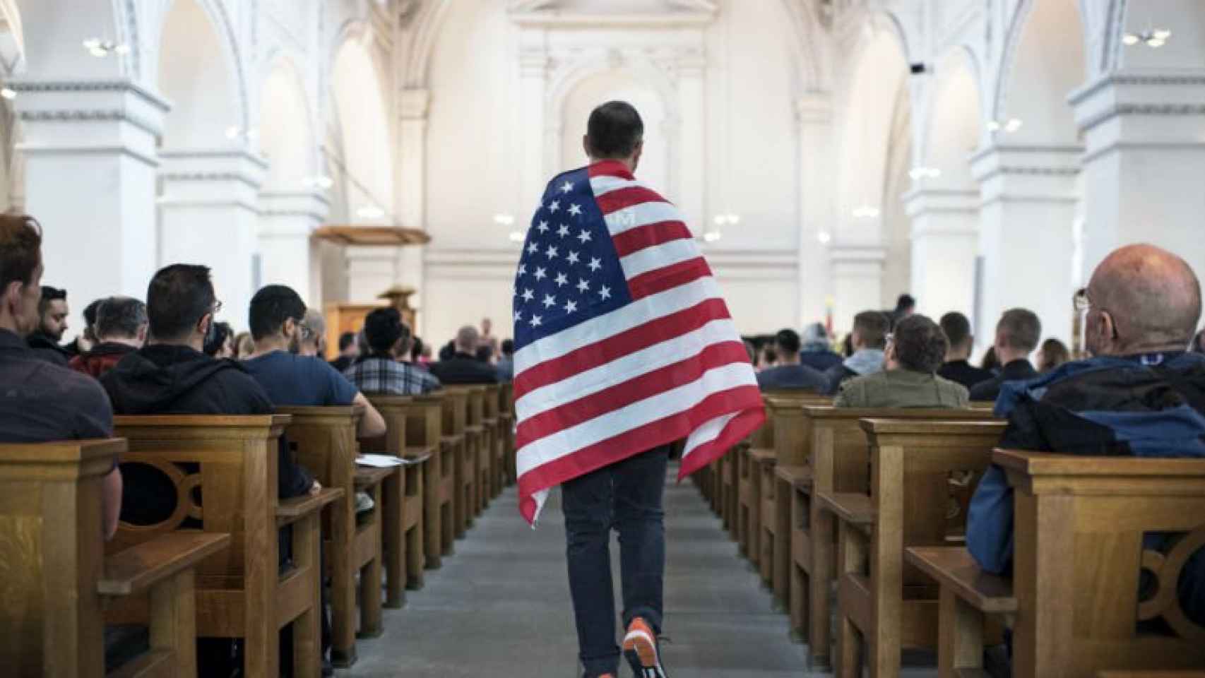 Un defensor de la comunidad de lesbianas, gais, bisexuales y transexuales (LGBT) porta una bandera estadounidense durante una vigilia por las 49 víctimas mortales, celebrada en una iglesia de Zúrich, Suiza.