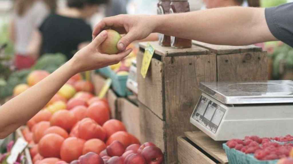 Uno de los comerciantes barceloneses entrega una pieza de fruta a un cliente en una imagen de archivo / EP