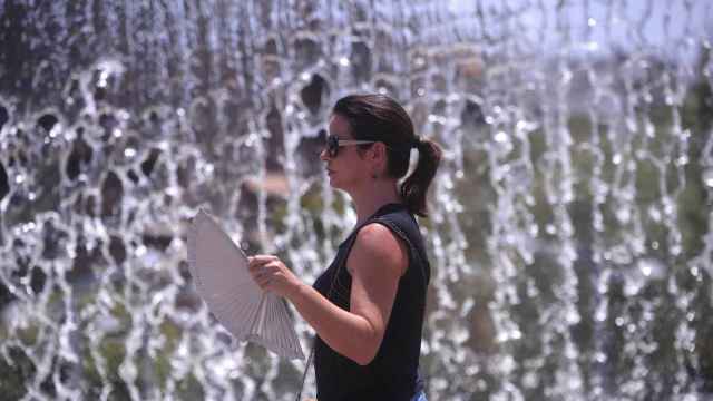 Una mujer sostiene un abanico al lado de una fuente en plena ola de calor / EFE