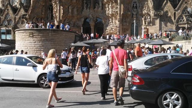 Turistas cruzan pasando entre los coches en la plaza de la Sagrada Familia / CG
