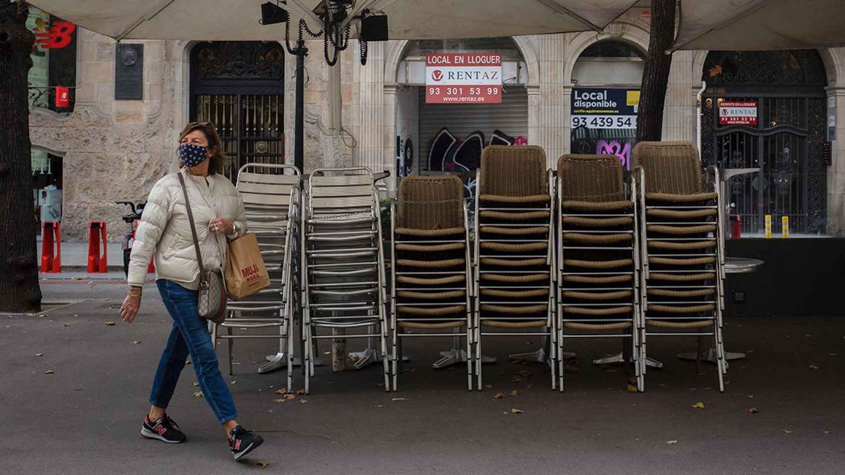 Una mujer pasa junto a la terraza recogida de un bar cerrado / EUROPA PRESS