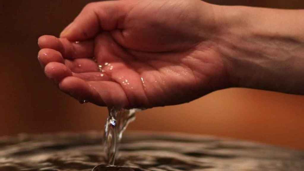 Una mano sumergida en agua bendita / PARROQUIA DE SANTA EULALIA