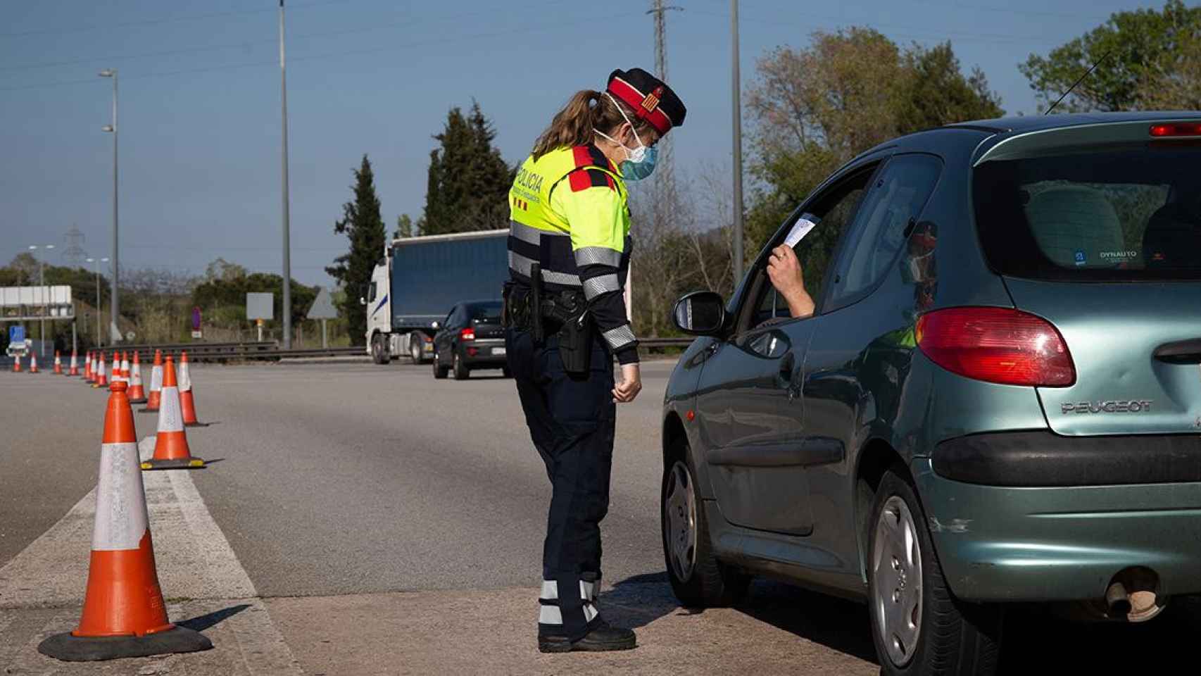 Una agente de los Mossos d'Esquadra protegida con una mascarilla en un control en el peaje de La Roca del Vallès pide a un conductor el justificante que le permite su salida de casa / EP