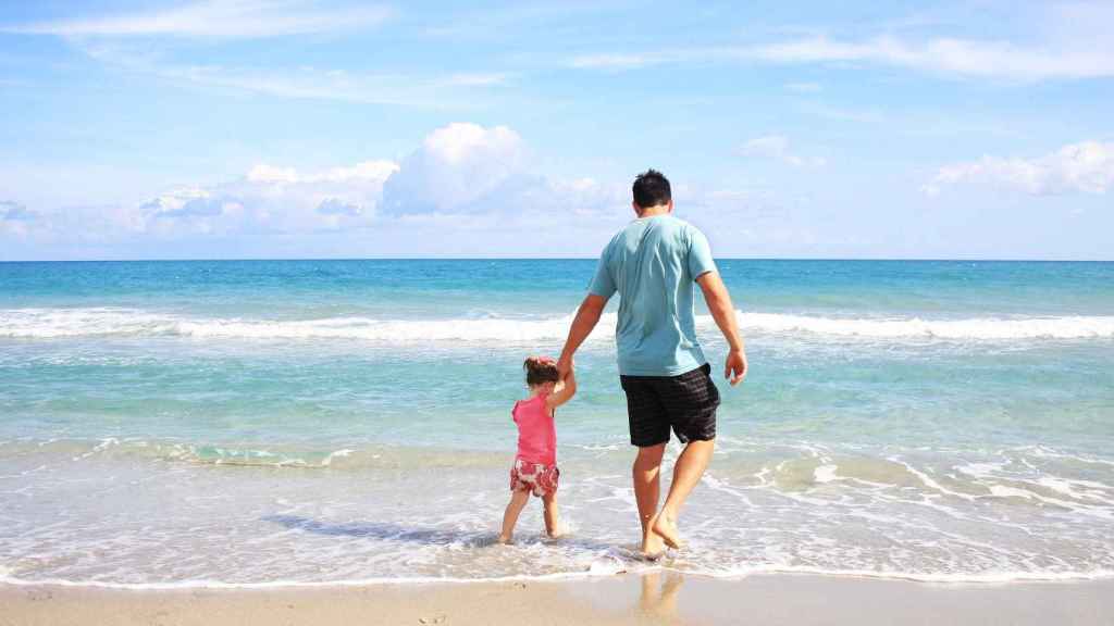 Un padre camina con su hija por la playa. Hay fotoprotectores especiales para cada miembro de la familia / PX