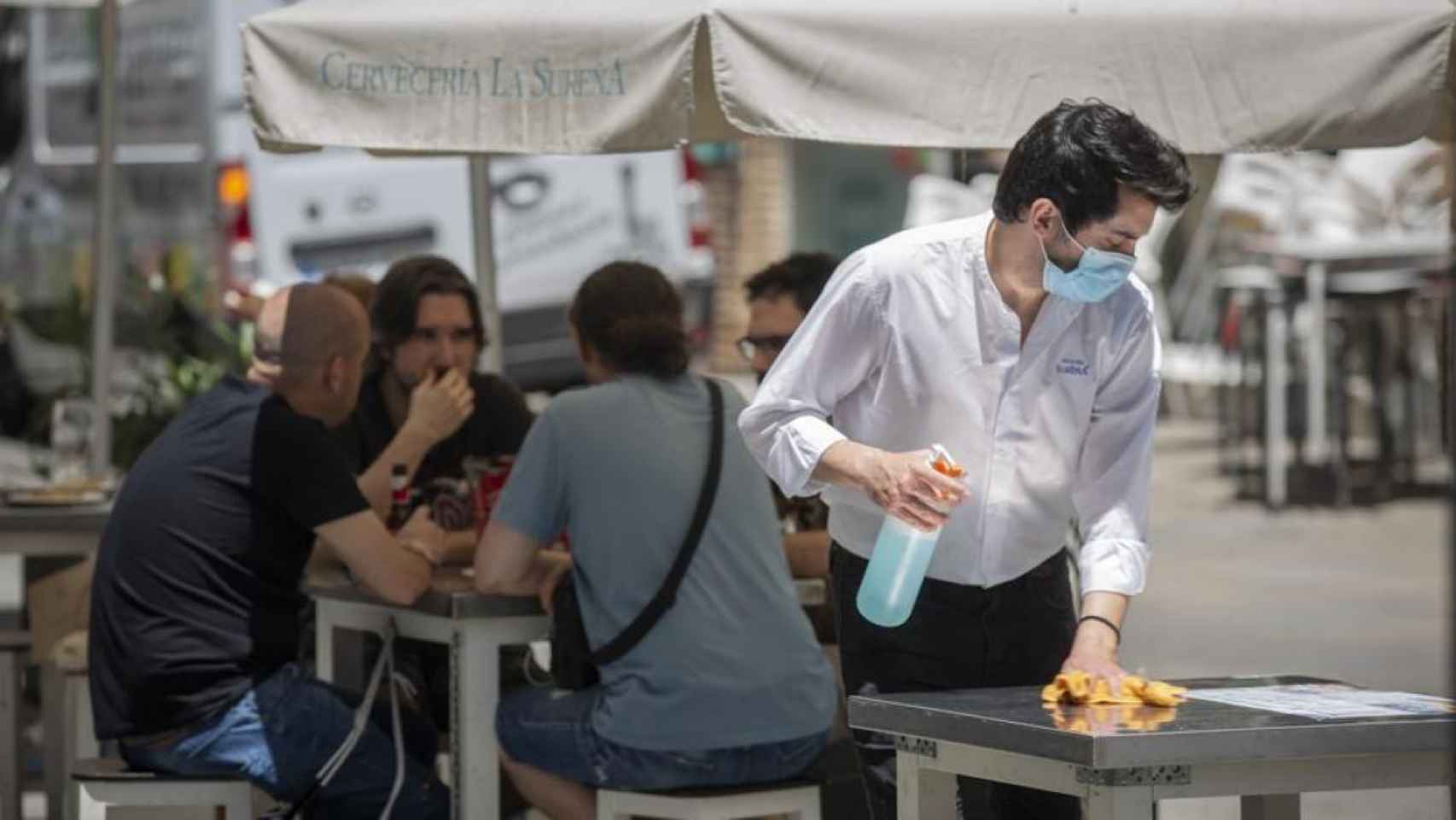 Un camarero con mascarilla limpia una mesa para evitar el contagio del Covid en superficies / EP