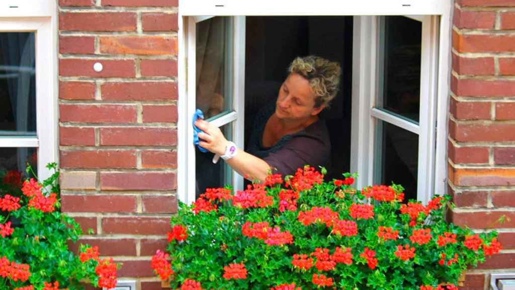 Una empleada de hogar limpia las ventanas de la casa donde trabaja