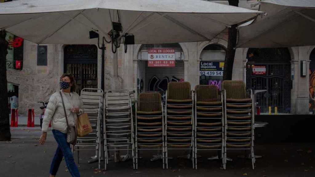 Una mujer pasa por delante de una terraza cerrada por las restricciones del Govern por la pandemia en Cataluña / EP