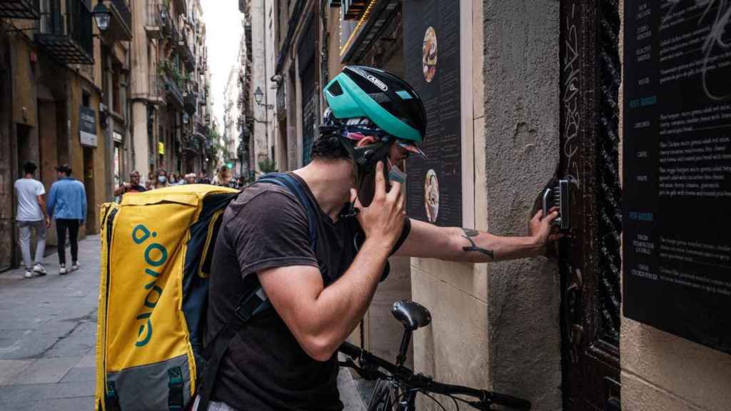 Javier Pérez, 'rider' de Glovo, llama a un cliente para que recoja su pedido en el barrio del Raval / PABLO MIRANZO