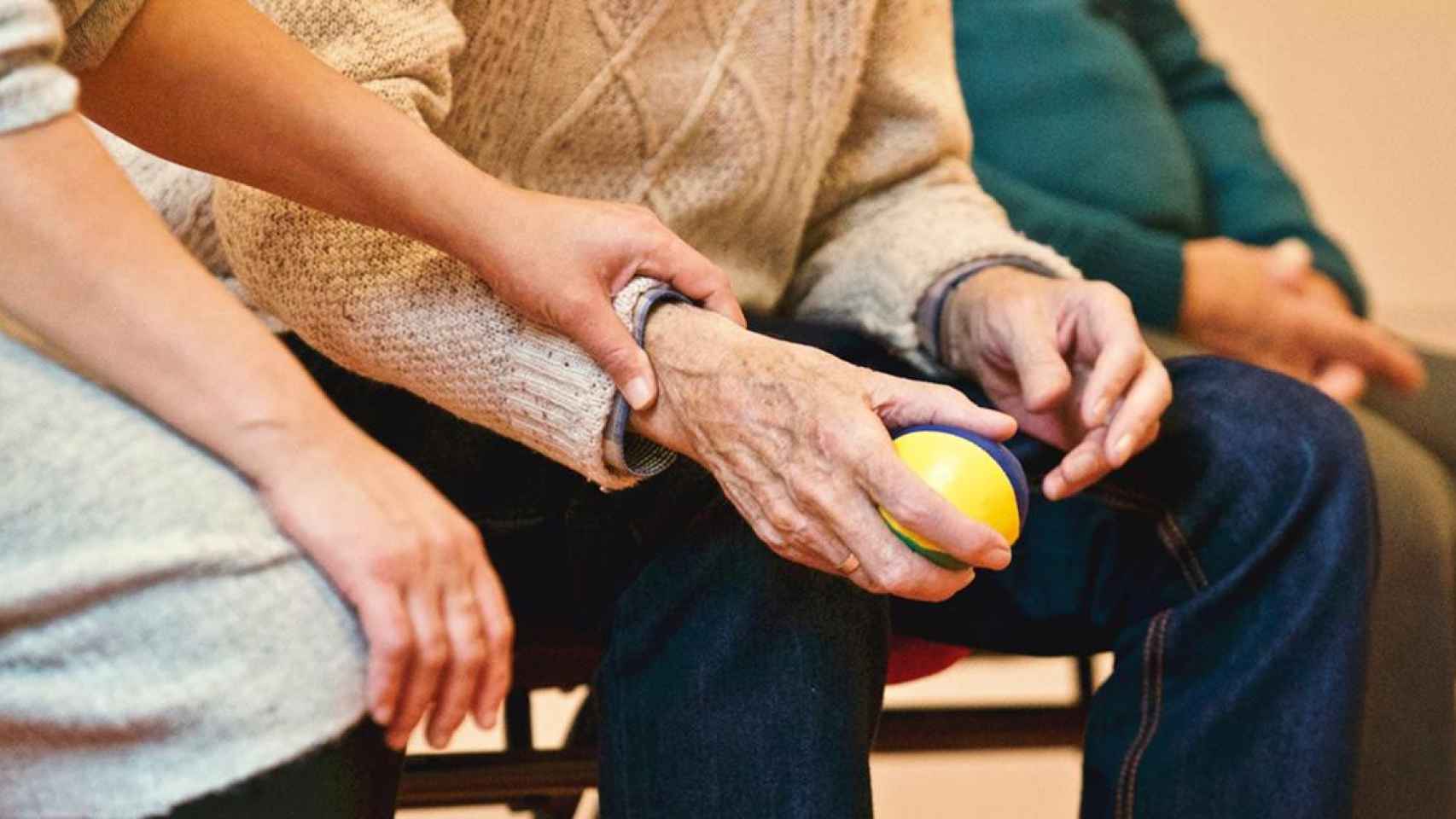 La mano de una trabajadora acaricia la de un anciano con alzheimer / EP (degradado)