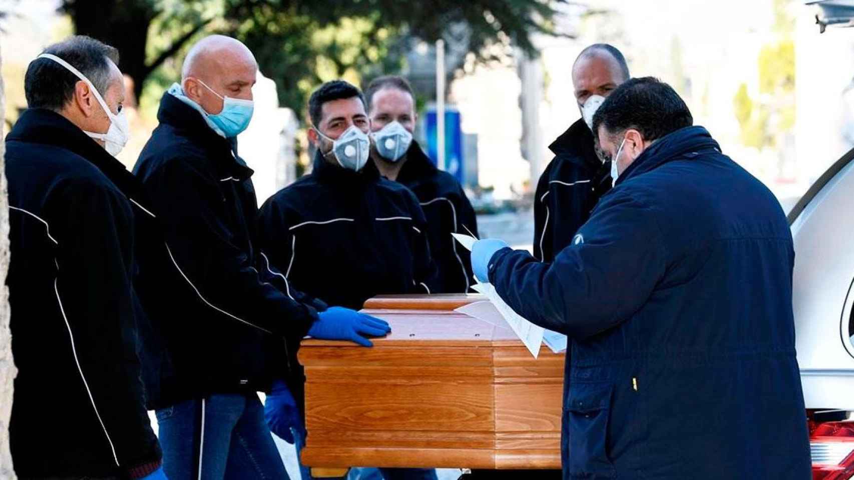 Imagen de operarios con mascarilla de una funeraria de Madrid trasladando un féretro / EFE