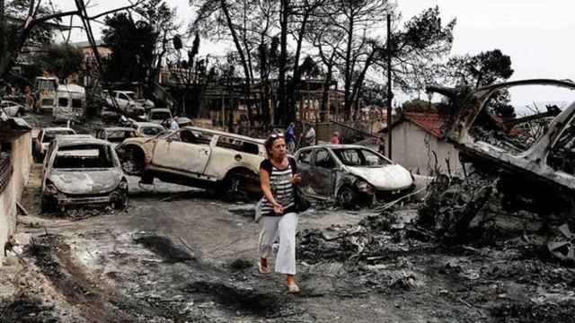 Una residente pasa entre los coches calcinados en Mati (Grecia) / EFE