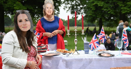 Personas con máscaras de la reina británica y la duquesa de Cambridge disfrutan de un picnic mientras participan en el Gran Almuerzo en el Largo Paseo durante las celebraciones del Jubileo de Platino de la reina Isabel II de Gran Bretaña, en Windsor, este domingo - EFE/ Neil Hall