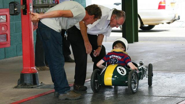 Un hombre mira cómo su hijo conduce un coche de juguete / CG