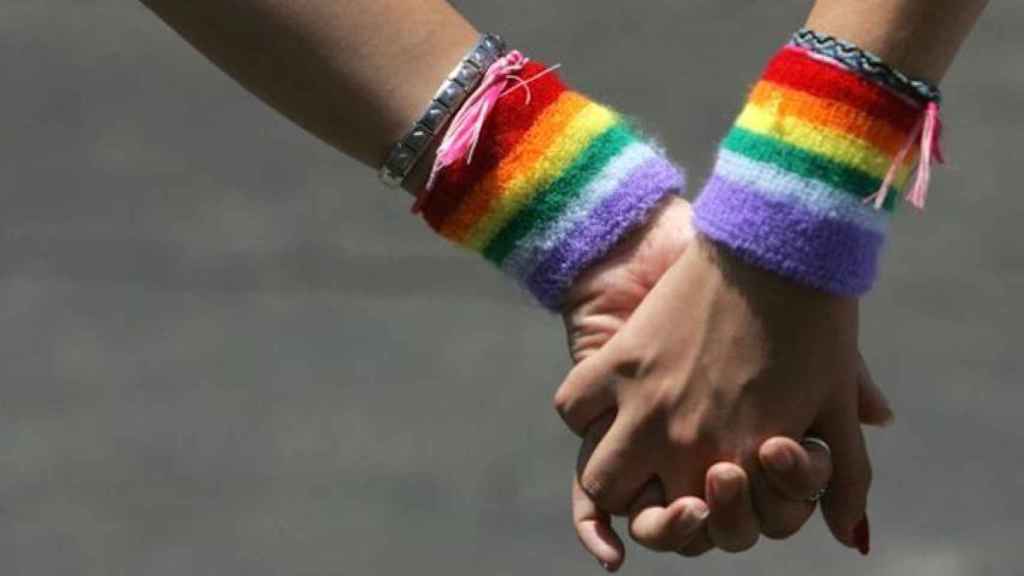 Dos chicas sujetan sus manos con los colores de la bandera gay