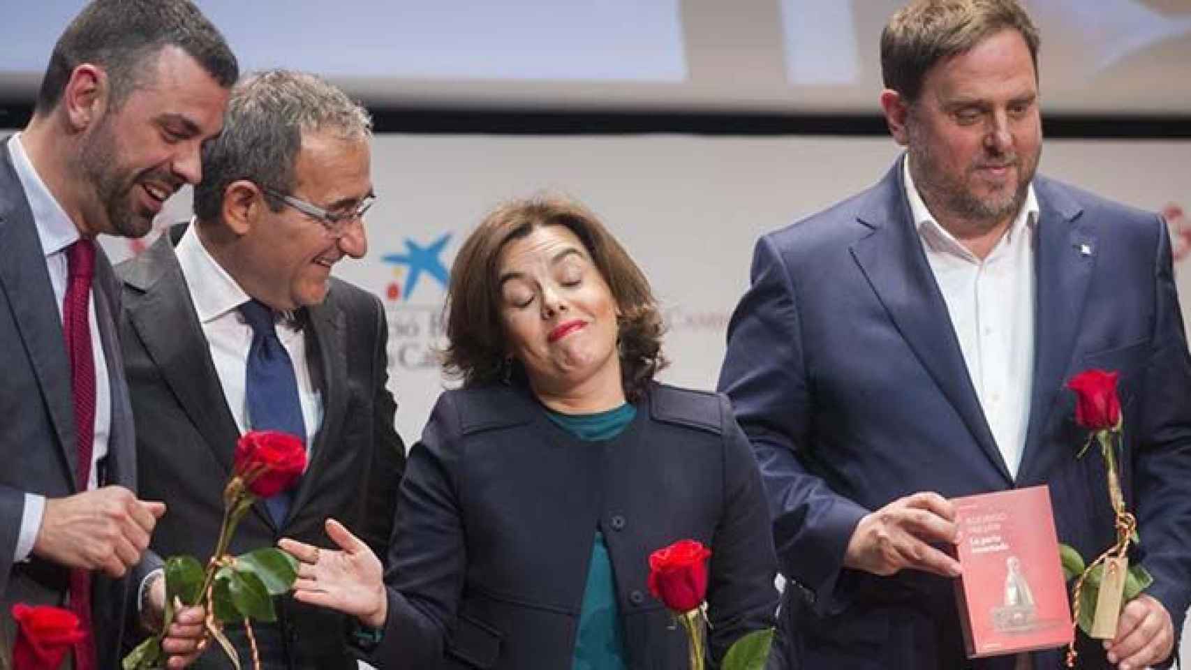 La vicepresidenta del Gobierno, Soraya Sáenz de Santamaria, regala un libro al vicepresidente de la Generalitat, Oriol Junqueras (d), en presencia del presidente del Gremio de Editores, Patrici Tixis, y el entonces 'conseller' de Cultura, Santi Vila (i) /